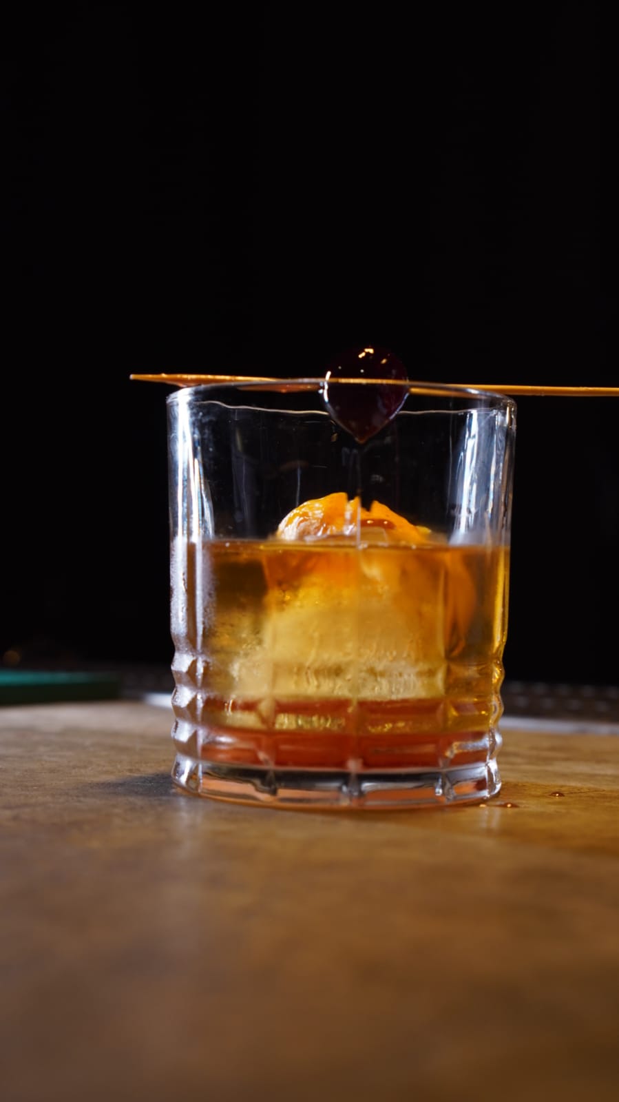 Drink âmbar servido com gelo e cereja